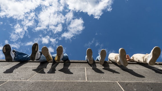 Vier Jugendliche lassen auf einer hohen Mauer ihre Beine baumeln. © picture alliance/dpa | Frank Rumpenhorst Foto: Frank Rumpenhorst