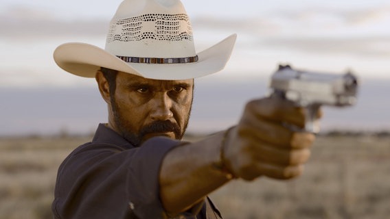 Ein Mann mit Cowboyhut richtet seine Waffe auf etwas. © IMAGO / Mary Evans 