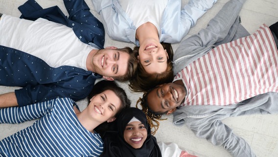 Fünf junge Menschen liegen mit den Köpfen in der Mitte auf dem Fußboden und bilden einen Stern. © picture-alliance / Zoona 