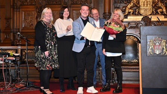 Gruppe von fünf Personen: Verleihung des Senator Neumann Preises an den NDR am 4. Dezember 2023 im Hamburger Rathaus. Die Preisträger René Schaar und Uschi Heerdegen-Wessel halten eine Urkunde. Mit dabei Hamburgs Zweite Bürgermeisterin Katharina Fegebank. Gruppe von fünf Personen: Verleihung des Senator Neumann Preises an den NDR am 4. Dezember 2023 im Hamburger Rathaus. Die Preisträger René Schaar und Uschi Heerdegen-Wessel halten eine Urkunde. Mit dabei Hamburgs Zweite Bürgermeisterin Katharina Fegebank. © FHH/BWFGB/Kirstin Hammerstein Foto: Kirstin Hammerstein