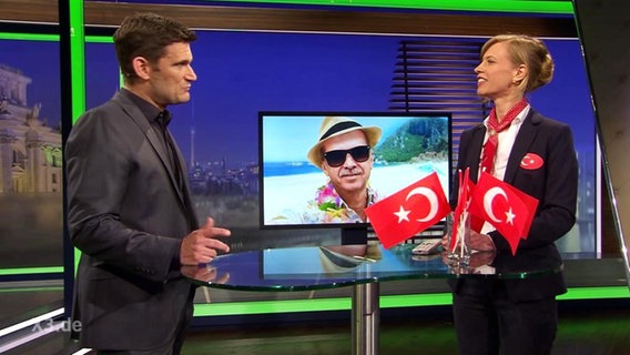 "Extra 3"-Moderator Christian Ehring steht zusammen mit einer Frau an einem Tisch mit Türkeiflaggen.  
