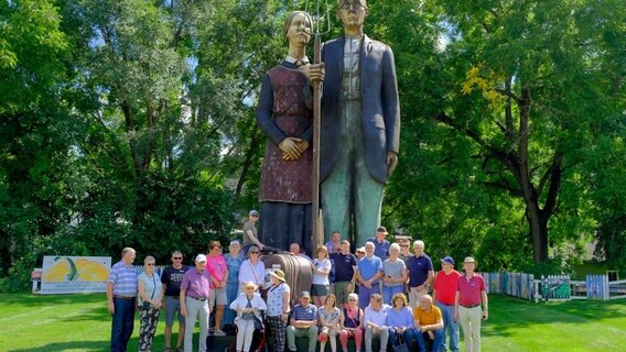 Die Reisegruppe in Anamosa Iowa vor einer Skulptur zur Erinnerung an den Künstler Grant Wood. © NDR/doc.station/Volkert Schult 