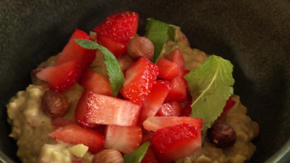 Eine Schüssel Frühstücksporridge mit Erdbeeren und Haselnüssen. © Screenshot 