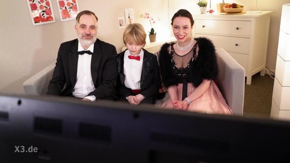 Ein gut gekleidete Familie sitzt vor einem Fernseher  