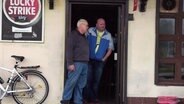 Zwei Männer lehnen im Eingang einer Kneipe.  