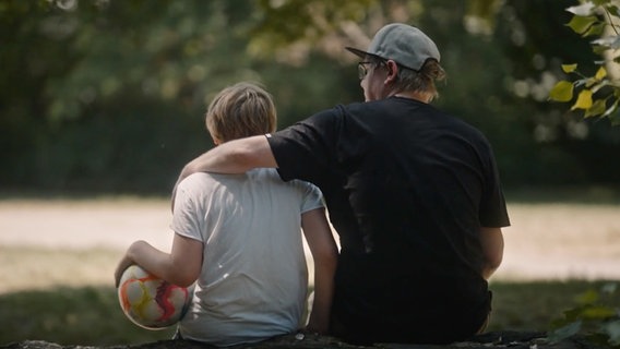 Philip sitzt neben seinem Sohn und legt einen Arm um ihn. © Drive Beta/Benjamin Kahlmeyer 