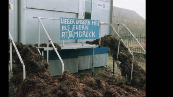 Mist vor einem Container, daran hängt ein Plakat mit der Aufschrift "Lieber unsern Mist als euern Atomdreck". © NDR 