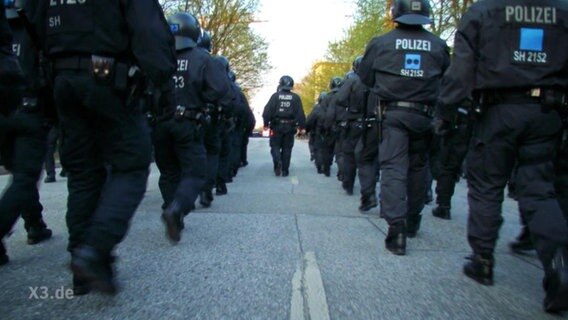 Eine Horde an Polizisten marschiert eine Straße dem Horizont entgegen.  