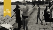 Schwimmer mit Bommelmütze zieht sich nach dem Wettkampf im Freibad schnell einen Bademantel über (1965).  