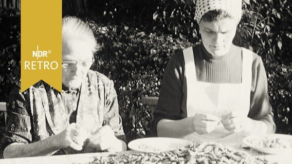Zwei Frauen sitzen an einem Tisch im Freien beim Krabbenpulen (1964)  