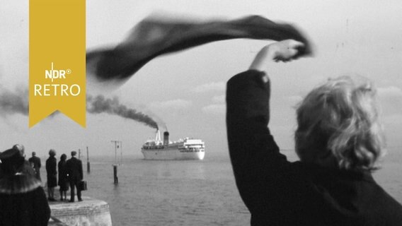 Eine Frau am Kai winkt mit dem Schal einem abfahrenden Fährschiff hinterher (1963)  