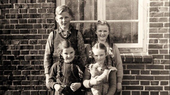 Vier Kinder stehen vor einem Haus.  