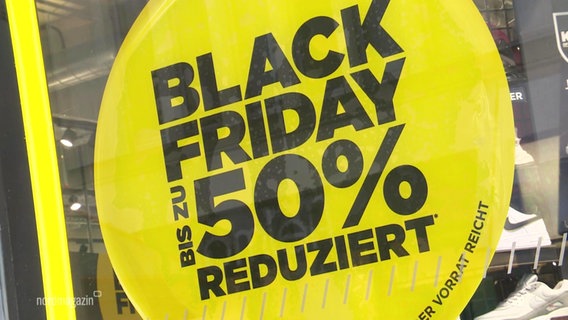 Auf einem gelben Aufkleber an einer Schaufensterscheibe steht "Black Friday, bis zu 50% reduziert".  