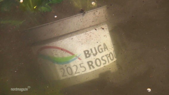 Ein Plastikbehälter mit der Aufschrift "BUGA 2025 Rostock" unter Wasser. © Screenshot 