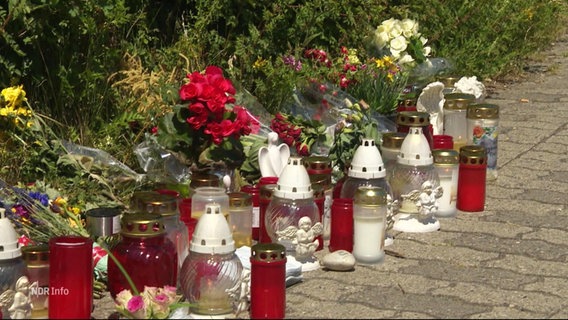 Am Rande eines Gehwegs sind mehrere Grabkerzen und Blumen aufgestellt. © Screenshot 
