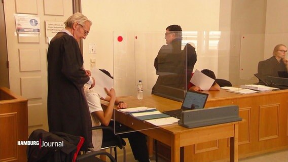 Zwei Angeklagte sitzen im Prozess um einen antisemitischen Angriff auf eine Mahnwache in Hamburg im Gerichtssaal. © Screenshot 