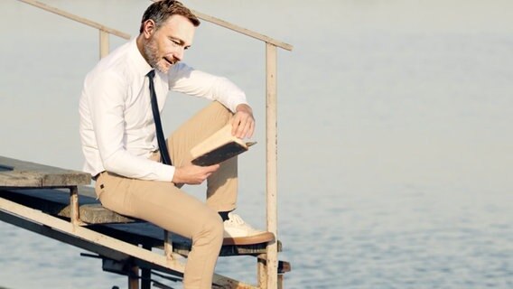 Christian Lindner sitzt an einer Treppe zum Meer und liest in seinem Tagebuch. © NDR 