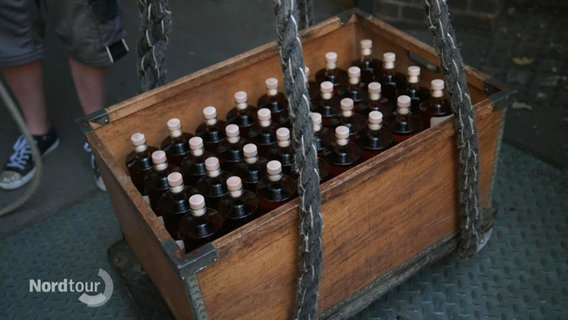 Auf dem Boden steht eine Kiste mit Rumflaschen die von dicken Tauen gehalten wird. © Screenshot 