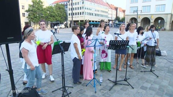 Der "Chor der Vielfalt" singt auf einem größeren Platz in Rostock. © Screenshot 