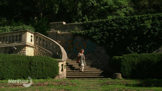 Eine Frau geht eine antik anmutende Treppe in einem römischen Garten hinab. © Screenshot 