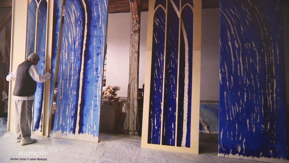 Der Künstler Günther Uecker steht vor seinen Entwürfen blauer Kirchenfenster. © Screenshot 