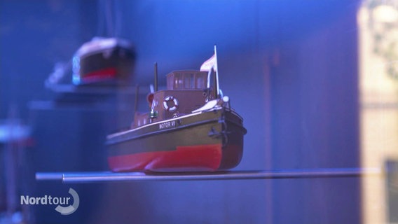 Ein Miniaturmodell eines Elbschiffs steht auf einer Glasplatte in einer Vitrine. © Screenshot 