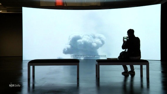 Eine Person sitzt vor einer Videoinstallation. © Screenshot 