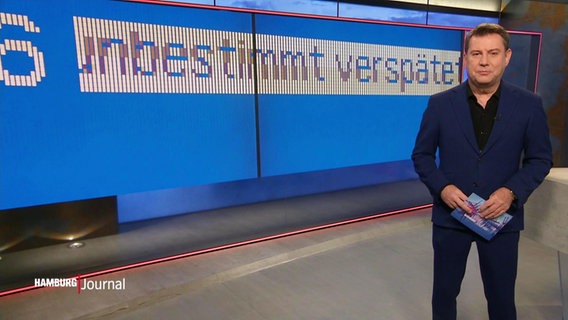 Jens Riewa moderiert das Hamburg Journal am 08.10.2022. Hinter ihm ist eine Anzeigetafel eingeblendet, die eine Zugverspätung ankündigt. © Screenshot 