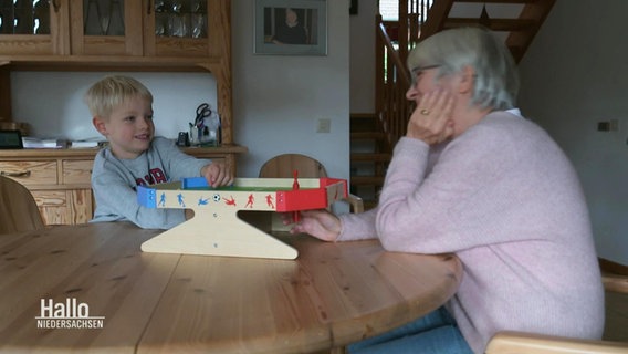 Ein Kind spielt mit einer älteren Frau ein Spiel am Küchentisch. © Screenshot 