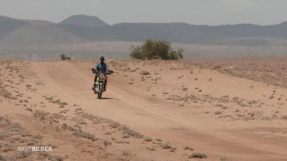 Ein Mann fährt Motorrad in einer sehr trockenen Gegend. © Screenshot 