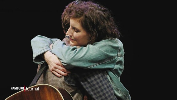 Ein Schauspieler und eine Schauspielerin umarmen sich auf einer Theaterbühne. © Screenshot 