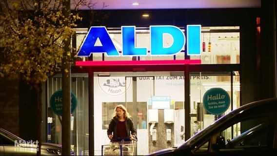 Eine Frau kommt mit einem Einkaufswagen aus einer ALDI-Filiale. Über ihr prngt das erleuchtete Logo der Ladenkette. © Screenshot 