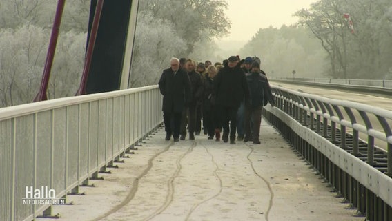 Ein Pulk von Menschen geht auf einer größeren Brücke bei Schnee auf die Kamera zu. © Screenshot 