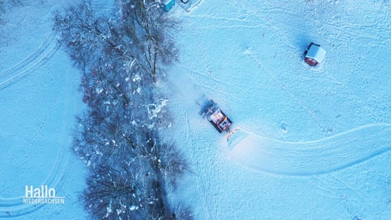 Blick aus der Vogelperspektive auf einen Schneepflug, der auf einer schneeweißen Piste eine Bahn zieht. © Screenshot 
