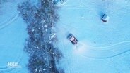 Blick aus der Vogelperspektive auf einen Schneepflug, der auf einer schneeweißen Piste eine Bahn zieht. © Screenshot 