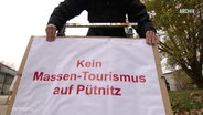 Eine Person hält ein Schild mit der Aufschrift: Kein Massentourismus auf Pütnitz. © Screenshot 