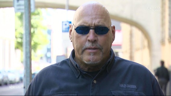 Der ehemalige Rocker-Boss Frank Hanebuth mit Sonnenbrille in einer Straße im Interview. © Screenshot 