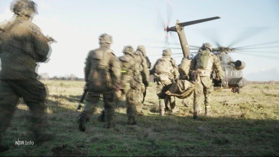 Auf einem Truppenübungsplatz geht eine Soldatentrupp auf einen gelandeten Kampf-Hubschrauber zu. © Screenshot 