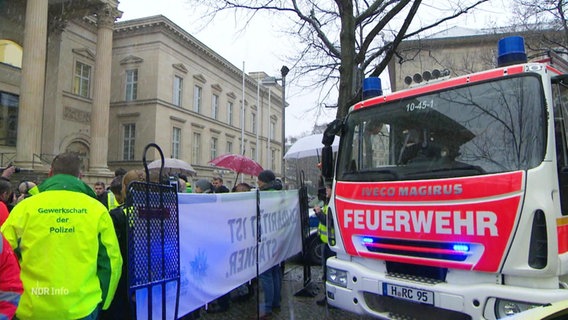 Ein Einsatzfahrzeug der Feuerwehr und Demonstrierende vor dem Landtag. © Screenshot 
