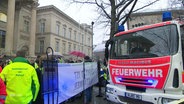 Ein Einsatzfahrzeug der Feuerwehr und Demonstrierende vor dem Landtag. © Screenshot 