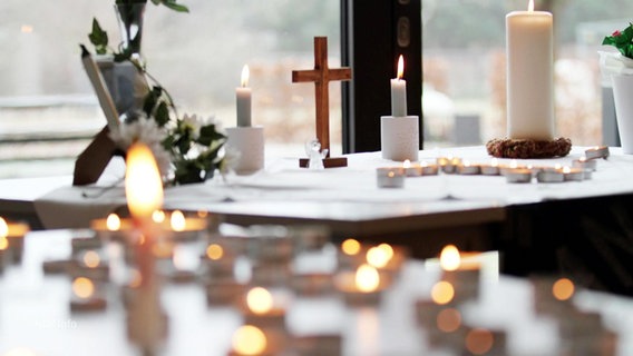 Ein Tisch mit Kerzen und Holzkreuz. © Screenshot 