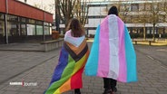Zwei Personen sind in Flaggen der LGBTQI+-Bewegung gehüllt. © Screenshot 
