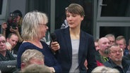 Bei einer Bürgerversammlung spricht eine Bürgerin in ein Handmikro, dass ihr von einer Freu hingehalten wird. © Screenshot 