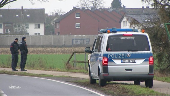 Am Rand einer Landstraße ist ein Einsatzfahrzeug der Polizei geparkt, daneben stehen zwei Beamte. © Screenshot 