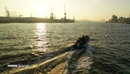 Ein Schnellboot fährt auf der Elbe, im Hintergrund sind Hafenkräne zu sehen. © Screenshot 