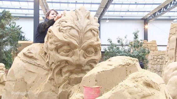 Eine Carverin fertigt eine Sandskulptur für die Ausstellung in Prora auf Rügen an. © Screenshot 