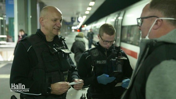 Zwei Bundespolizisten sprechen mit Zugreisenden auf einem Bahngleis. © Screenshot 