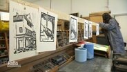 Mehrere Drucke hängen zum Trocknen in einer Werkstatt. © Screenshot 