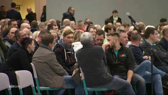 Viele Menschen sitzen bei einer Bürgerversammlung in Stuhlreihen in einer Turnhalle. © Screenshot 