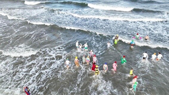 Menschen in bunten Klamotten gehen im Meer schwimmen © Screenshot 